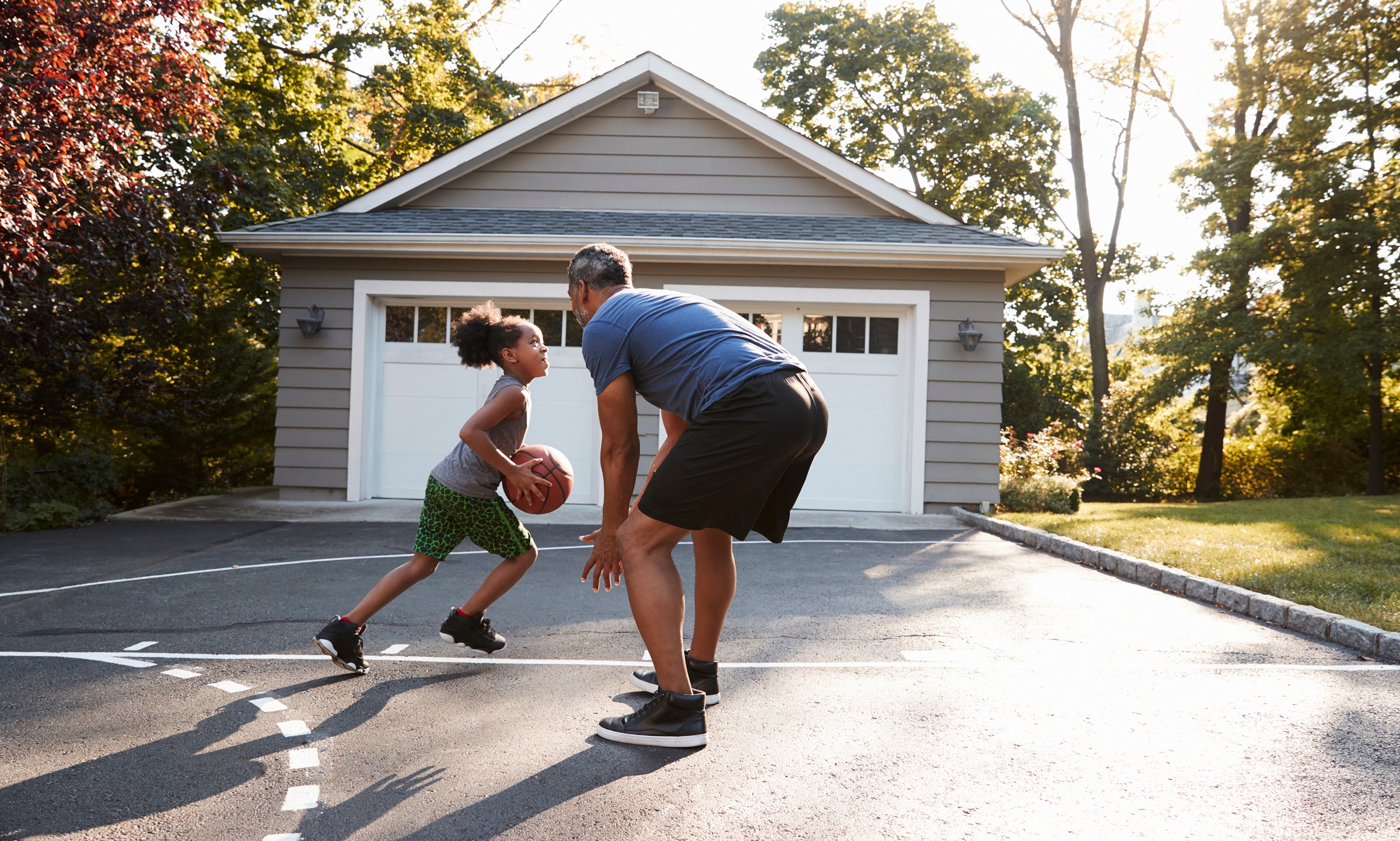 Father and child playing basketball together in a residential driveway.