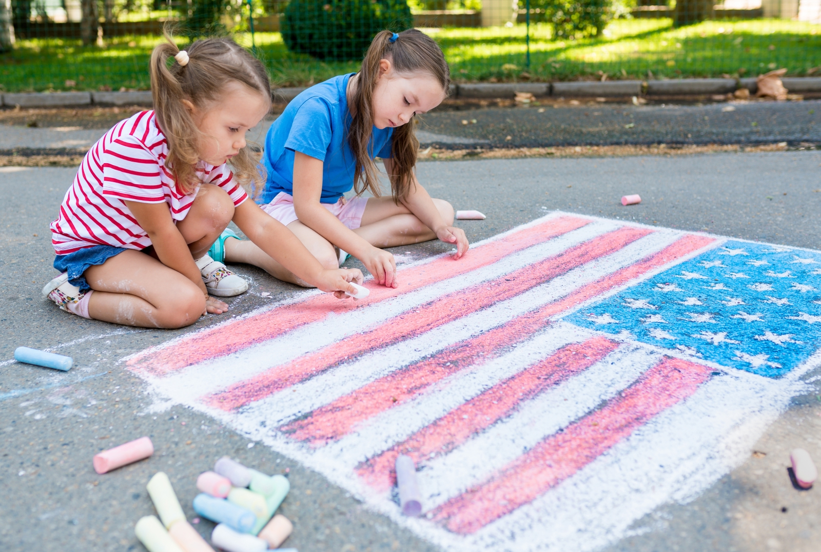 Two children drawing an American flag with sidewalk chalk outdoors.