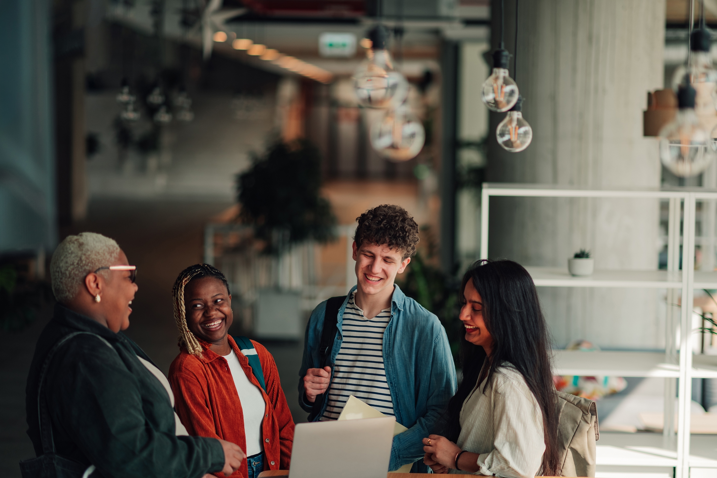 Diverse group of people talking and laughing together in a modern indoor workspace.