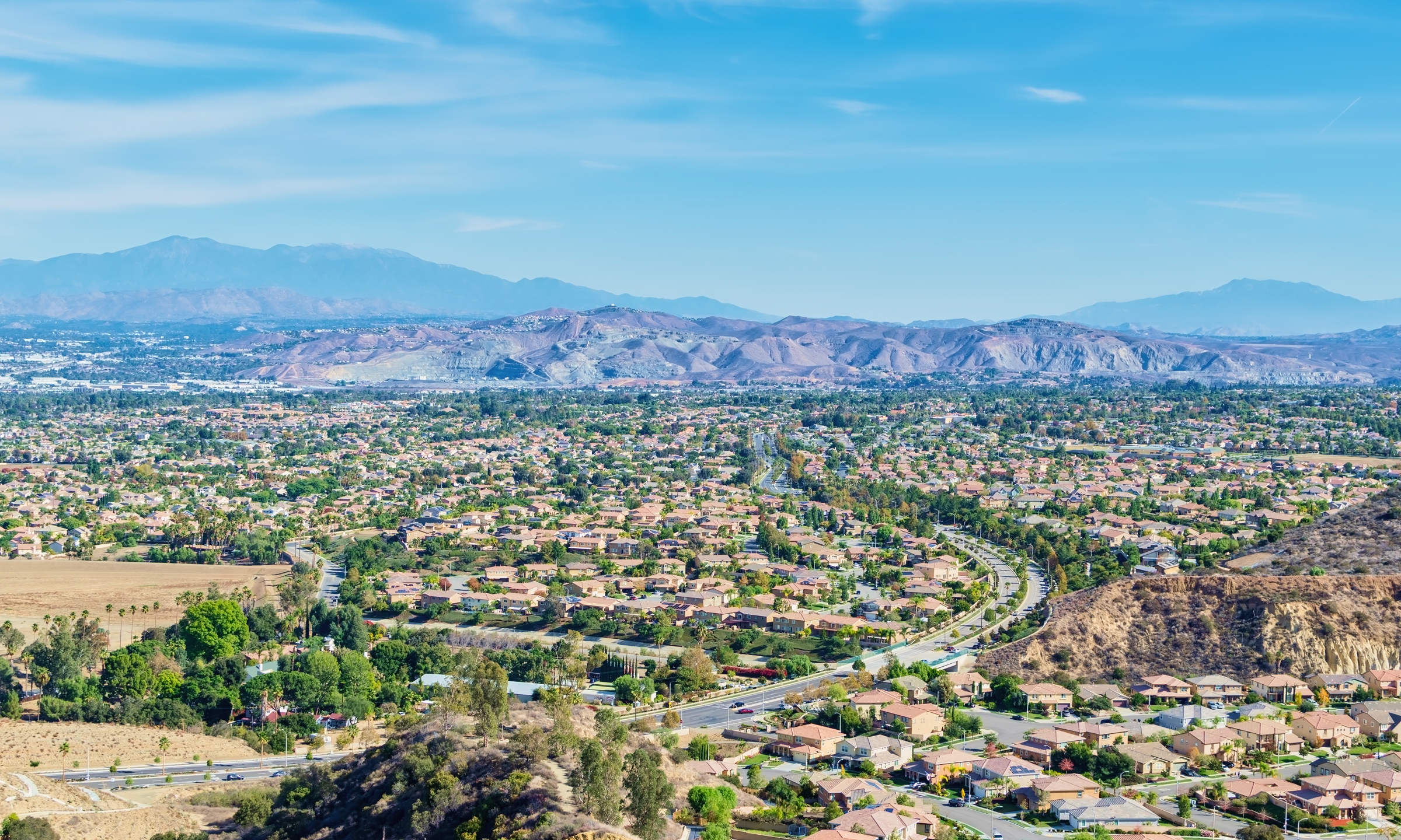 Panoramic view of a suburban neighborhood with tree-lined streets and mountains in the background.
